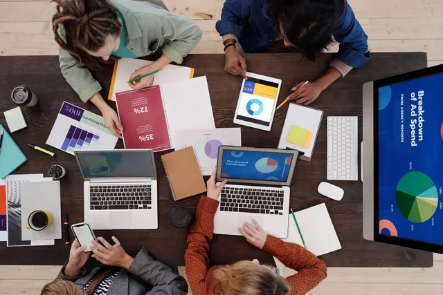 A diverse team collaborating on digital marketing strategies at a desk, using laptops and tablets. A programmatic advertising channel strategy should be scored, not argued