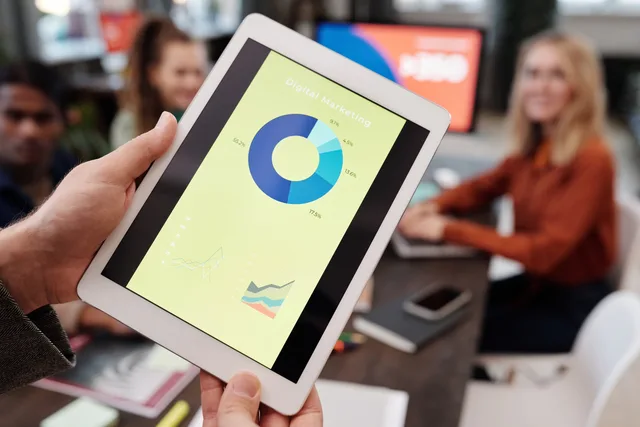 Business team reviewing digital marketing statistics on a tablet during an indoor meeting. CPM or retainer? Programmatic advertising pricing models compared