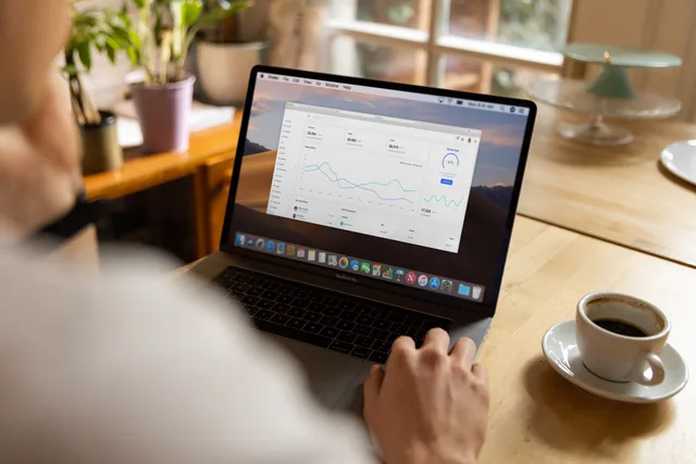 Person analyzing stock market data on laptop indoors with a casual setting and coffee. Programmatic advertising surveys: Brand Lift vs SurveyMonkey and Qualtrics
